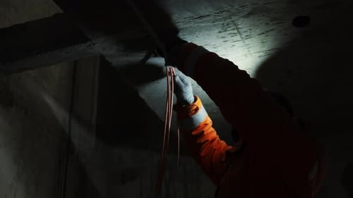 Construction Worker Inspecting Wires on Concrete Ceiling Indoors