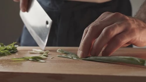 Front View of Young Chef Cutting Thin Slices of Green Onion with a Knife