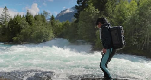 Female Traveler with a Backpack Drinking Water in Nature in the Forest Near a Mountain River