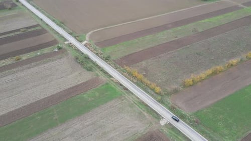 Drone aerial flyover brown green farmland black car driving through overcast