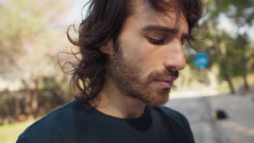Young Sad Long Hair Man Reads A Book In The Park Outdoors