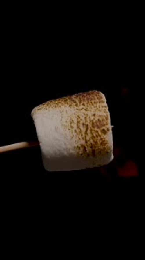 Vertical video. Marshmallow Rotating Slowly with Fire Flames on Black Background, close up, Isolated