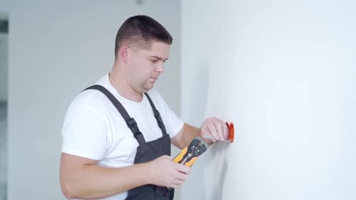 Male worker professional qualified electrician installs electrical outlet in apartment after repair.