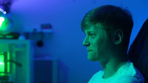 Closeup Side View of Cheerful Young Male Gamer Playing Online Computer Video Game in Dark Room