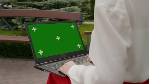 Woman sitting in the park with green screen laptop.