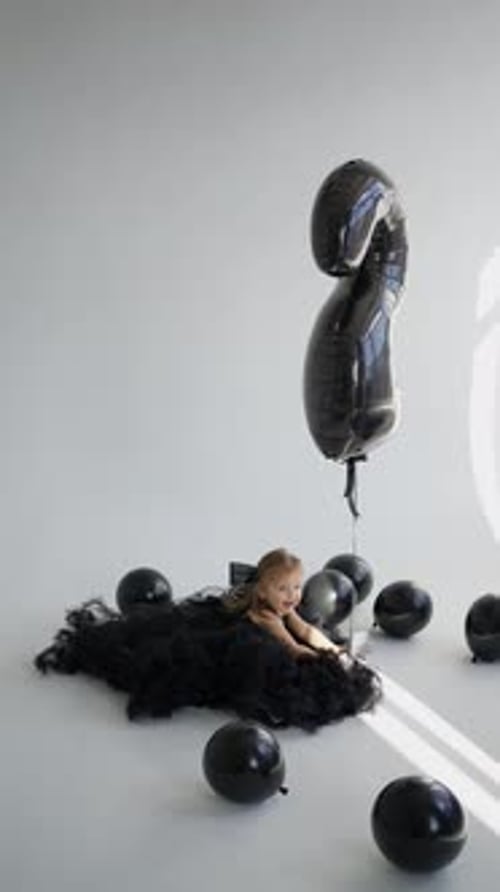 Adorable Girl Lying with Black Birthday Balloons