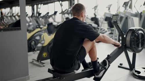 Young Man Training Intensely on Rowing Machine at Modern Gym