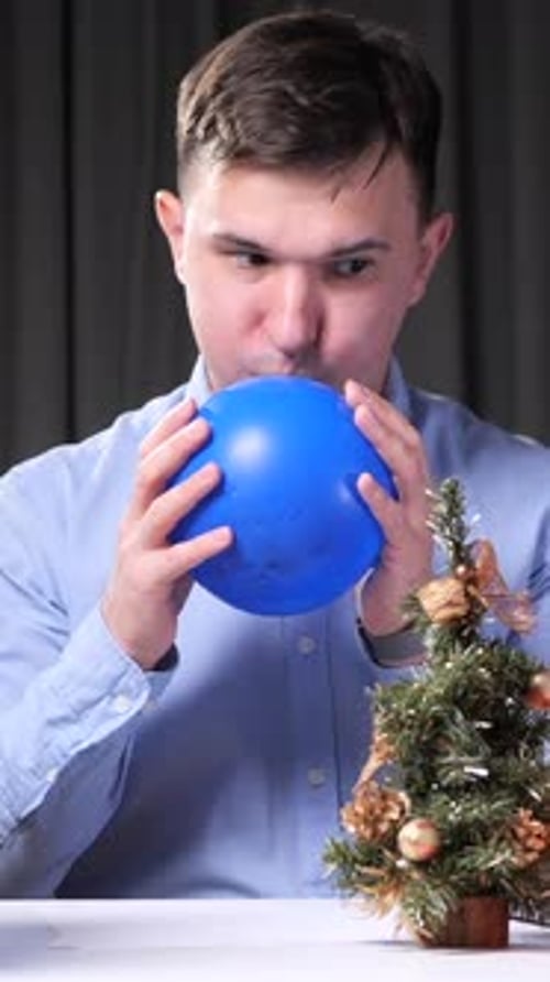 Vertical Video Office Worker Inflating Blue Balloon at Desk with Christmas Tree