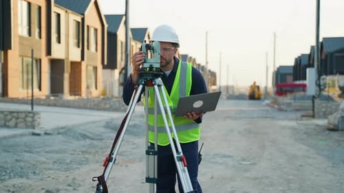 Surveyor Engineer Using Theodolite and Laptop on Construction Site