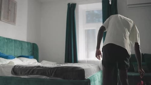 Person Walking with Bag in Modern Bedroom with Green Velvet Headboard and Soft Light