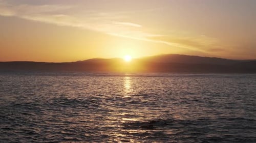 Brilliant sunset casts a radiant golden glow across the ocean, the sun dipping behind silhouetted
