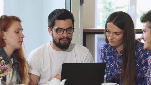 Friends Gathered Around a Laptop at a Cozy Coffee Shop Enjoying Breakfast
