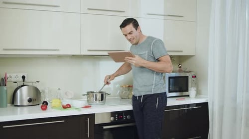 Man Cooking Soup Reading Recipe on Tablet in Kitchen