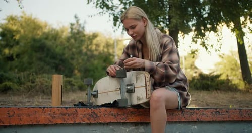 Young Woman Repairs Skateboard in Urban Skate Park