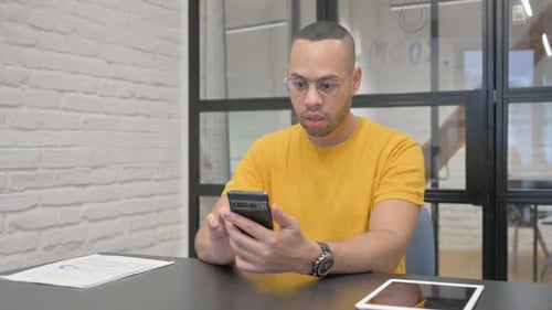 Hispanic Man Celebrating Success on Phone in Office