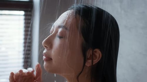 Woman Cleansing Face Under Shower Water in Bathroom