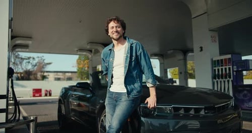 Man Smiles Leaning on Car at Gas Station