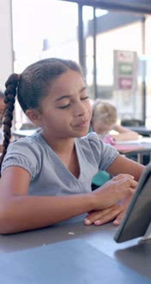 Vertical video: In school, young girl with a braid focusing on a tablet