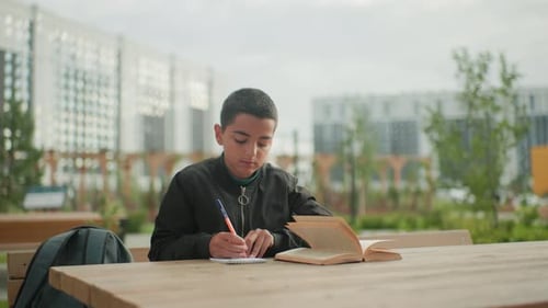 Young Kid Studying Outdoors with Book and Residential Building Background