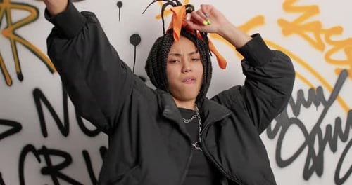 Stylish young woman dancing in front of graffiti wall