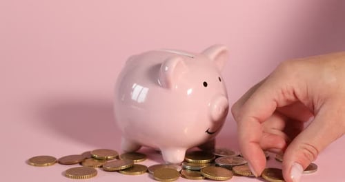 Financial savings. Woman putting coin into piggy bank on pink background, closeup