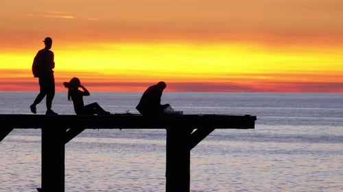 Silhouettes of People on the Sea Pier at Sunset