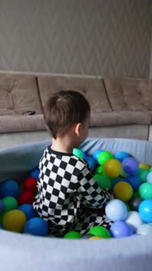 Happy joyful baby boy in checkered pajamas sits inside the dry pool at home.
