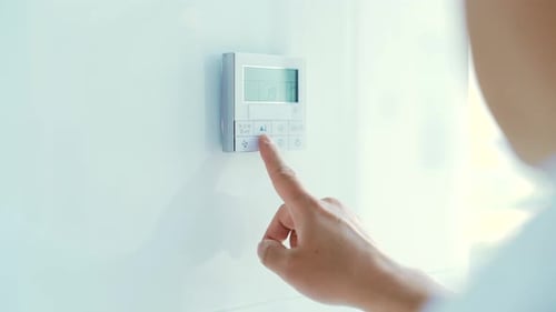 Hand Adjusting Digital Thermostat on Wall