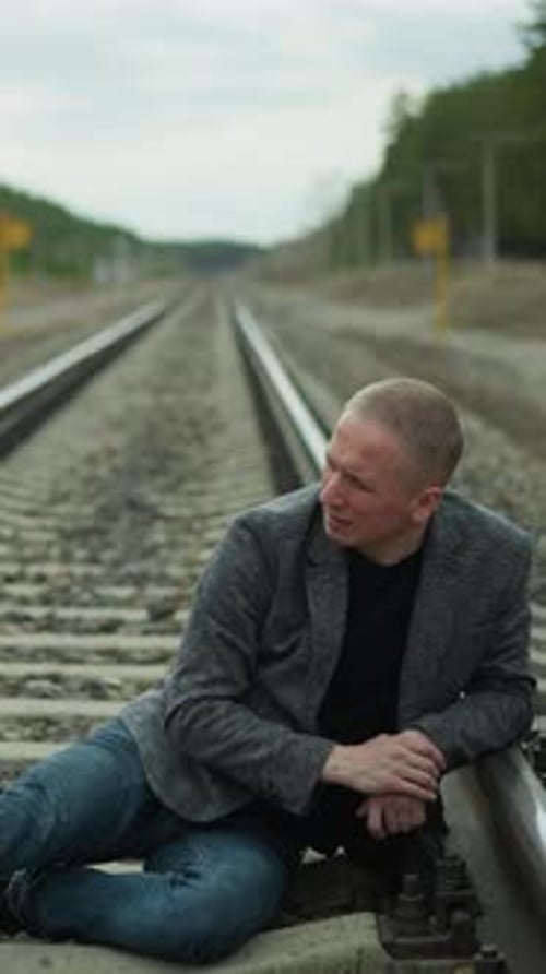 Man Sitting on Railroad Tracks Looking Sad