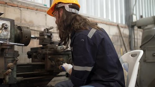 Blue collar worker is working at machine shop with welding robot arm.