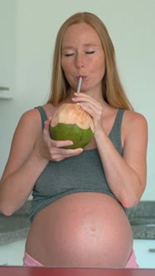 Femme enceinte heureuse buvant une jeune noix de coco dans une cuisine lumineuse Grossesse joyeuse mode de vie sain