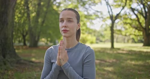 A Young Beautiful White Girl Practices Yoga in the Park and Meditates in the Lotus Position Among