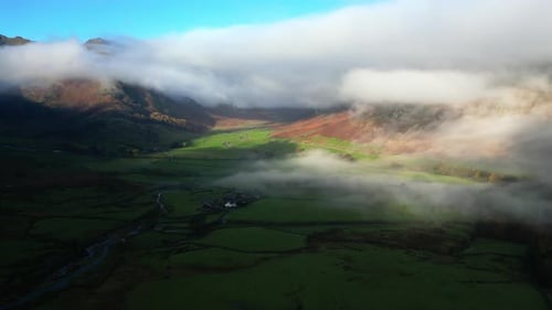 Shadowed green valley surrounded by cloud shrouded mountains lit by early morning autumn sunlight. C