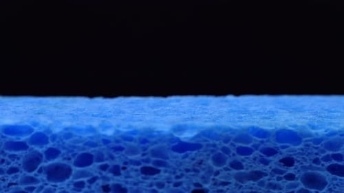 Close up of green dish washing liquid gel pouring on blue sponge on black background