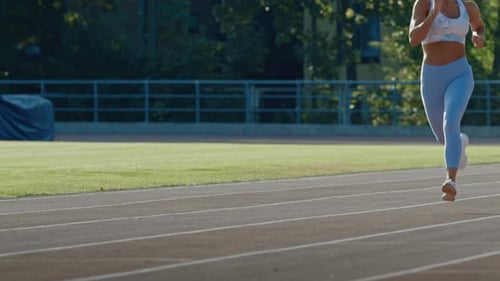 Schöne Fitnessfrau in hellblauem athletischem Top und Leggings beim Joggen in einem Stadion. Sie läuft