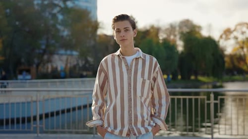 Man Standing Outside Keeps Hands in the Pockets on the Street and Looking at the Camera Portrait of
