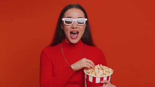 Femme excitée dans des lunettes 3D mangeant du pop-corn et regardant une série télévisée intéressante, un jeu de sport, un film