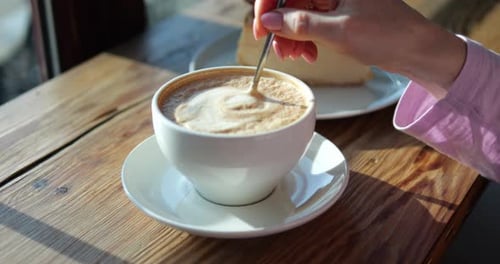 Stirring Cappuccino with Cheesecake on Wooden Table