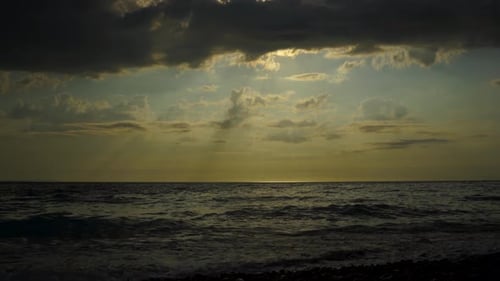 Dramatic seascape with dark clouds covering sunset and sun rays reflecting on sea surface
