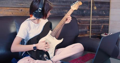 Teen Plays Electric Guitar with Headphones and Laptop