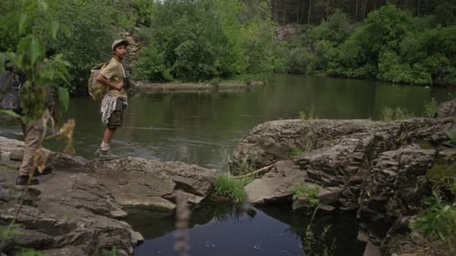 African American Father and Son with Backpacks Walking on River Bank
