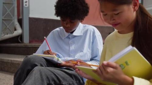Menino afro-americano e garota asiática fazendo a lição de casa no pátio da escola