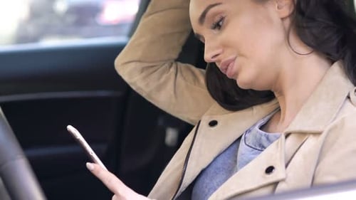 Young woman texts on her smartphone while sitting in a car on a road trip