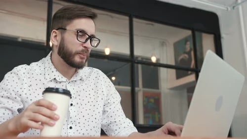 Mann arbeitet im Büro am Laptop und trinkt Kaffee