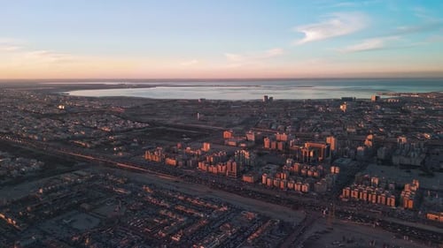 Golden Hour-Drohnenaufnahme der Skyline der Küstenstadt, des geschäftigen Autobahnverkehrs und der Bucht