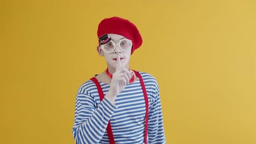 Der Typ Mime in einem gestreiften und hellen Kostüm und Make-up bringt seinen Zeigefinger auf seine Lippen und