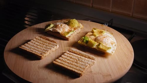 A close up shot as a chef carefully places cooked egg and avocado onto 4 slices of toasted brown bre