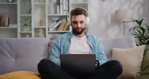 Casque sans fil pour homme d'affaires assis sur un canapé utilisant un ordinateur portable à la maison, jeune homme créatif