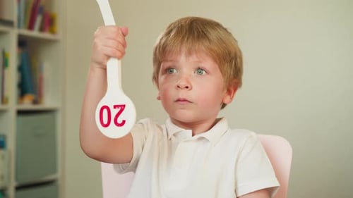 Boy Holding a Paddle with Red Numbers Indoors