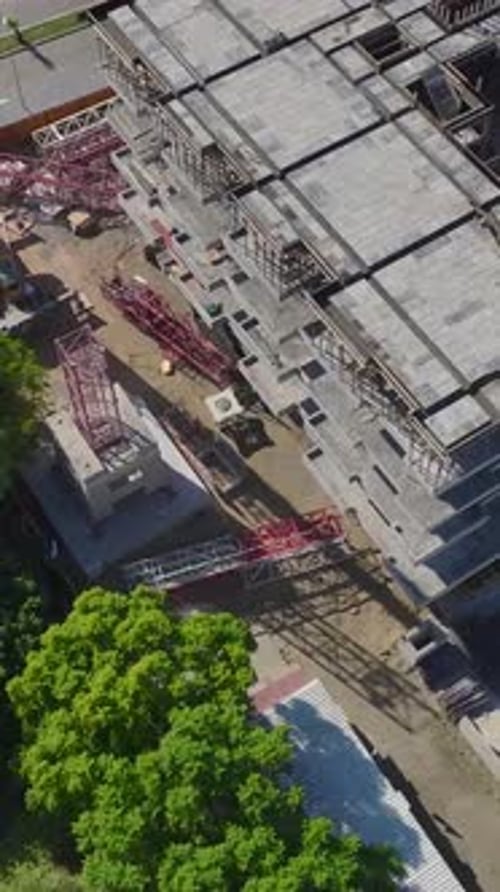 Vertical Video Aerial View Of Skilled Engineers Assembling A Tower Crane On A Vibrant Construction